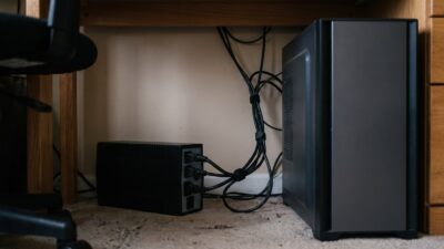 Malý čierny záložný zdroj UPS na podlahe pod pracovným stolom s pripojenými napájacími káblami